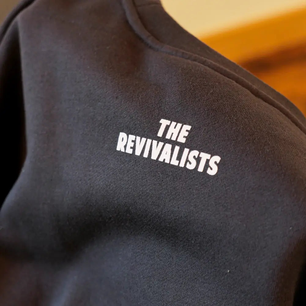 Black cotton sweatshirt with white embroidered text reading ’the revivalists’ across the shoulder.