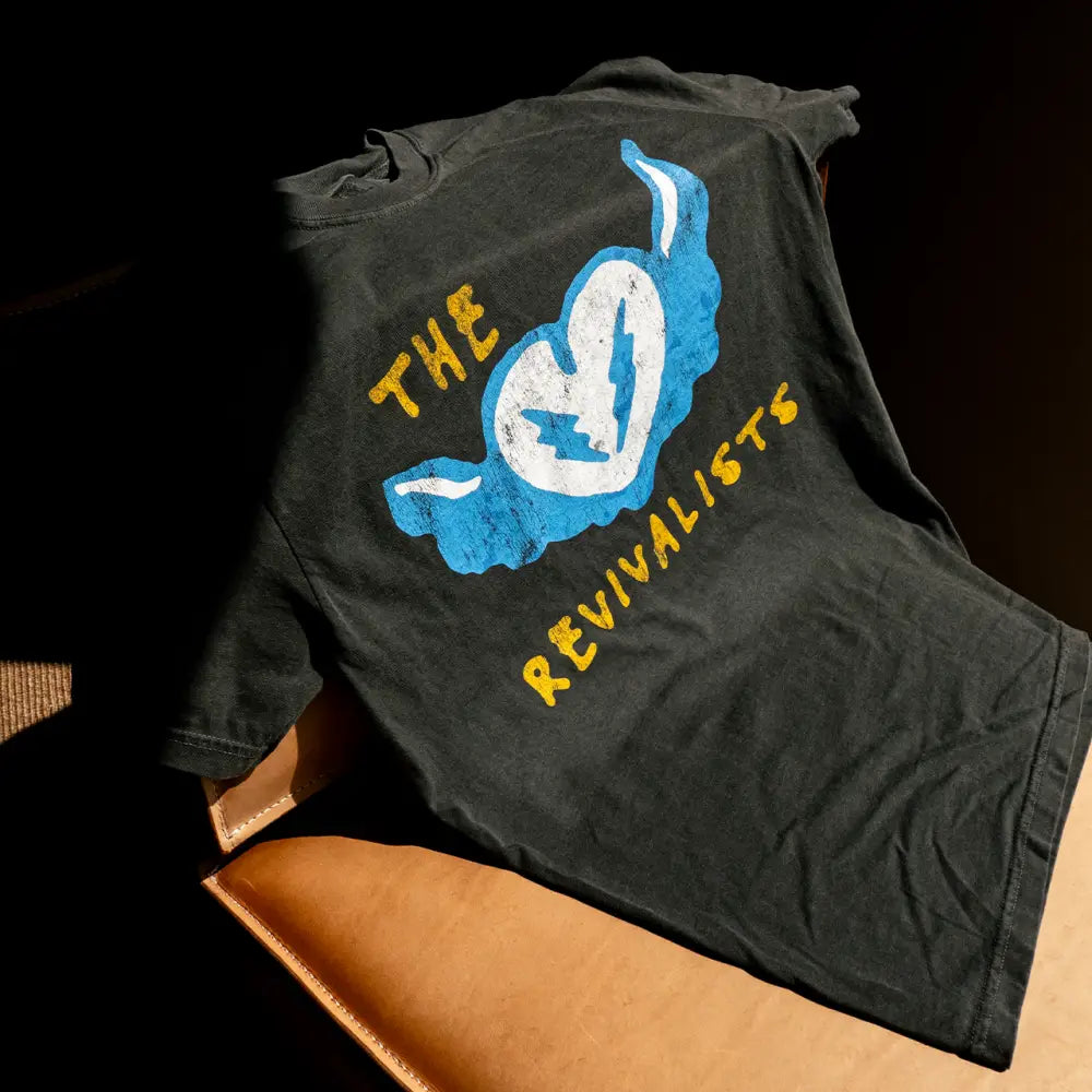 Black cotton heart stop tee featuring a distressed blue and white heart graphic with lightning bolts and yellow revivalists text