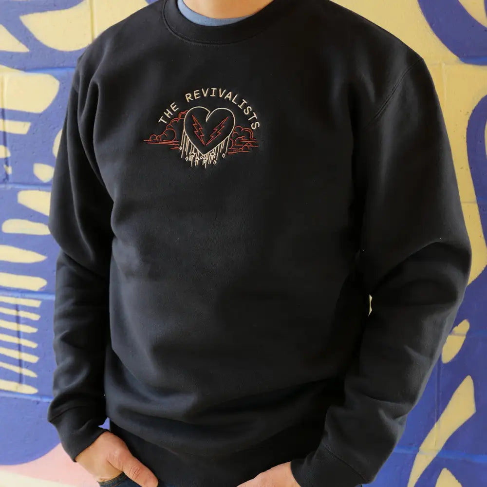 Black sweatshirt with a heart-shaped graphic design and text reading ’THE REVIVALISTS’.