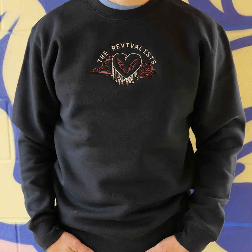 Black sweatshirt featuring a heart logo with wings and the text ’The Revivalists’ above it.