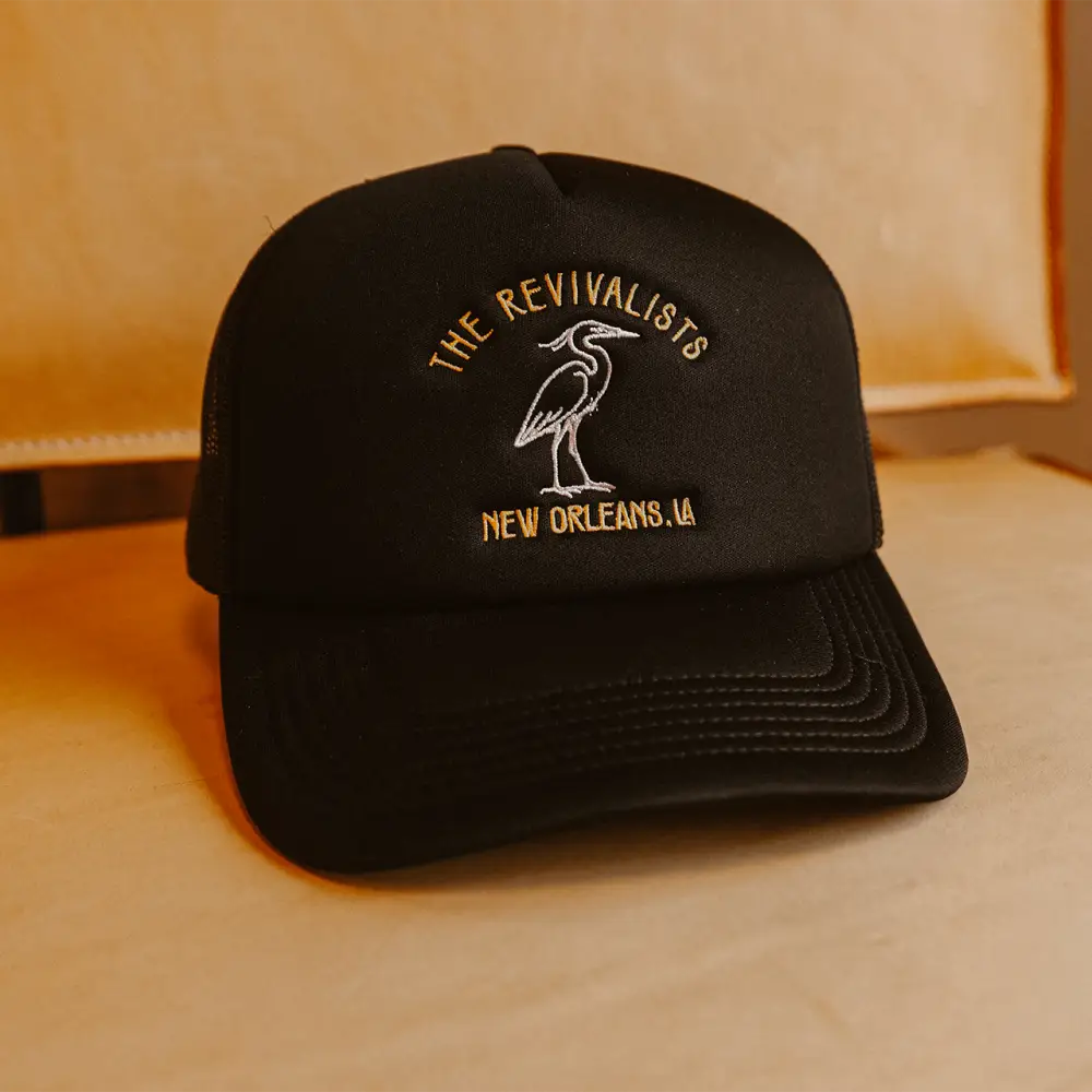 Black pelican hat trucker style with embroidered gold and white heron logo for the revivalists new orleans la