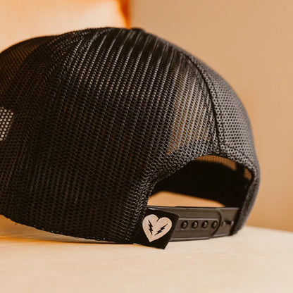 Black mesh pelican hat showing back strap with heart-shaped logo patch on adjustable trucker cap