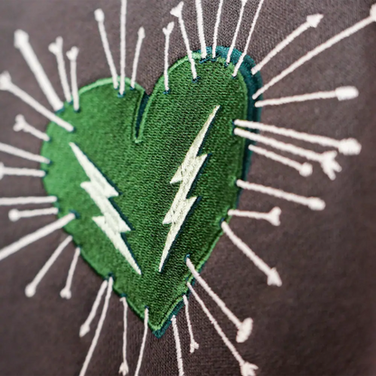 Green heart-shaped patch with white embroidered lightning bolts and radiating arrows.